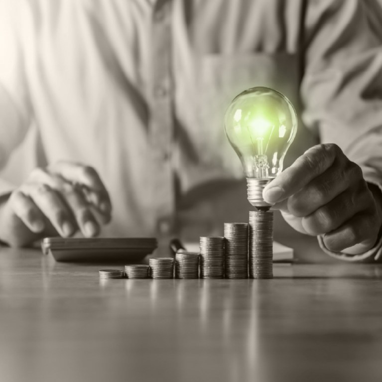 stacks of coins in rising order with a bright green light bulb on highest stack