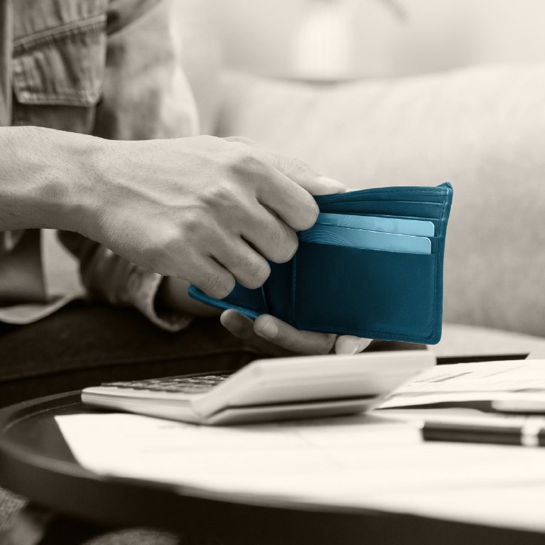 hand holding a blue wallet next to a calculator and some papers