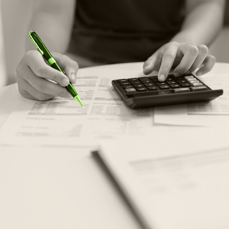 hand writing with a green pen to calculate budget with calculator