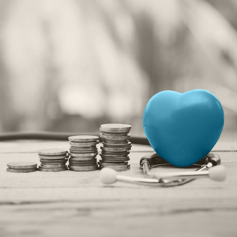 blue heart wrapped by a stethoscope on a desk with money
